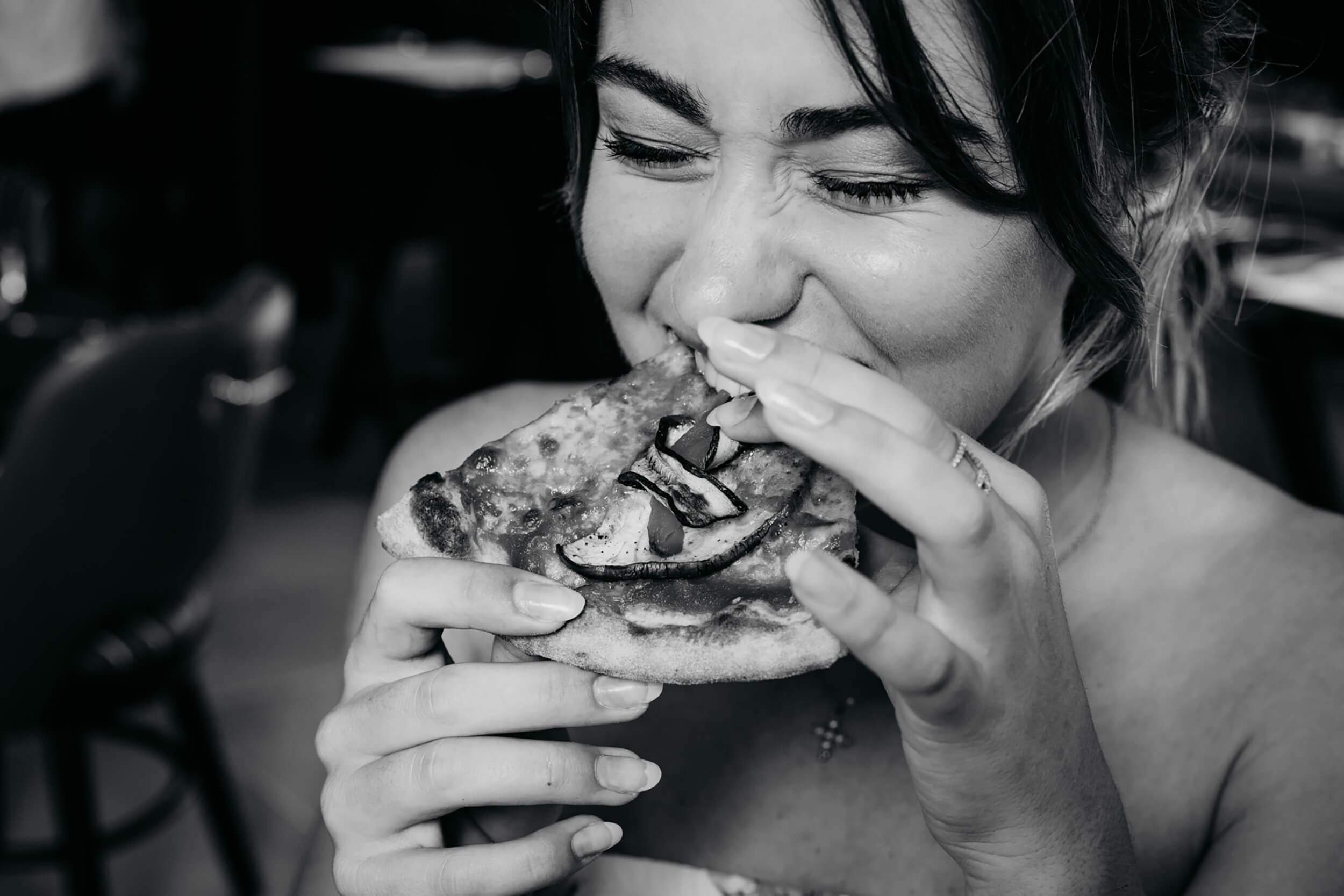 Woman taking a bite out of a pizza. The image is black and white.